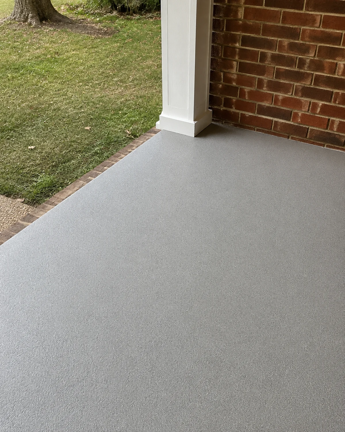 Textured porch coating at a threshold beside brick and a white post